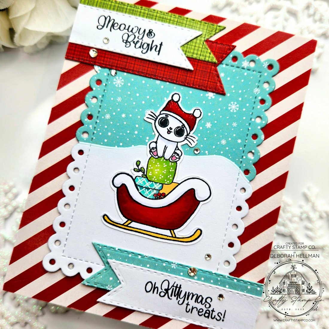Handmade Christmas card featuring a cute kitty in a sleigh with peppermint striped background and snow scene, created by Deborah using the Meowy Kittymas stamp set for Crafty Stamp Co.