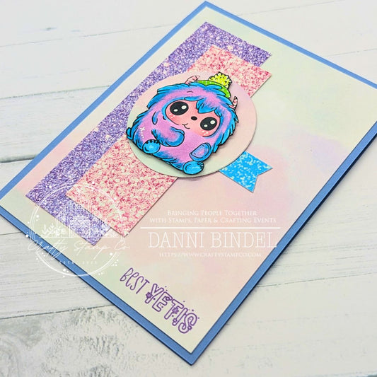 Colorful handmade card by Danni Bindel featuring a cute blue and purple yeti from Crafty Stamp Co.’s Yeti for Winter stamp set, layered over pastel glitter strips and the sentiment “Best Yetis.”