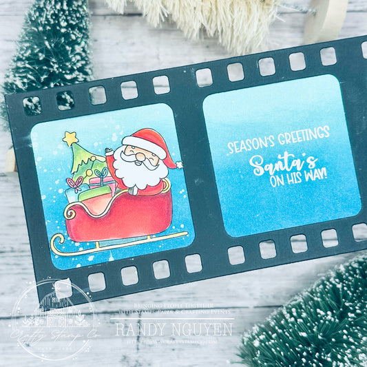 Handmade Christmas card featuring Santa in a sleigh, a sentiment reading “Season’s Greetings — Santa’s On His Way,” and a movie reel layout designed by Randy Nguyen for Crafty Stamp Co.