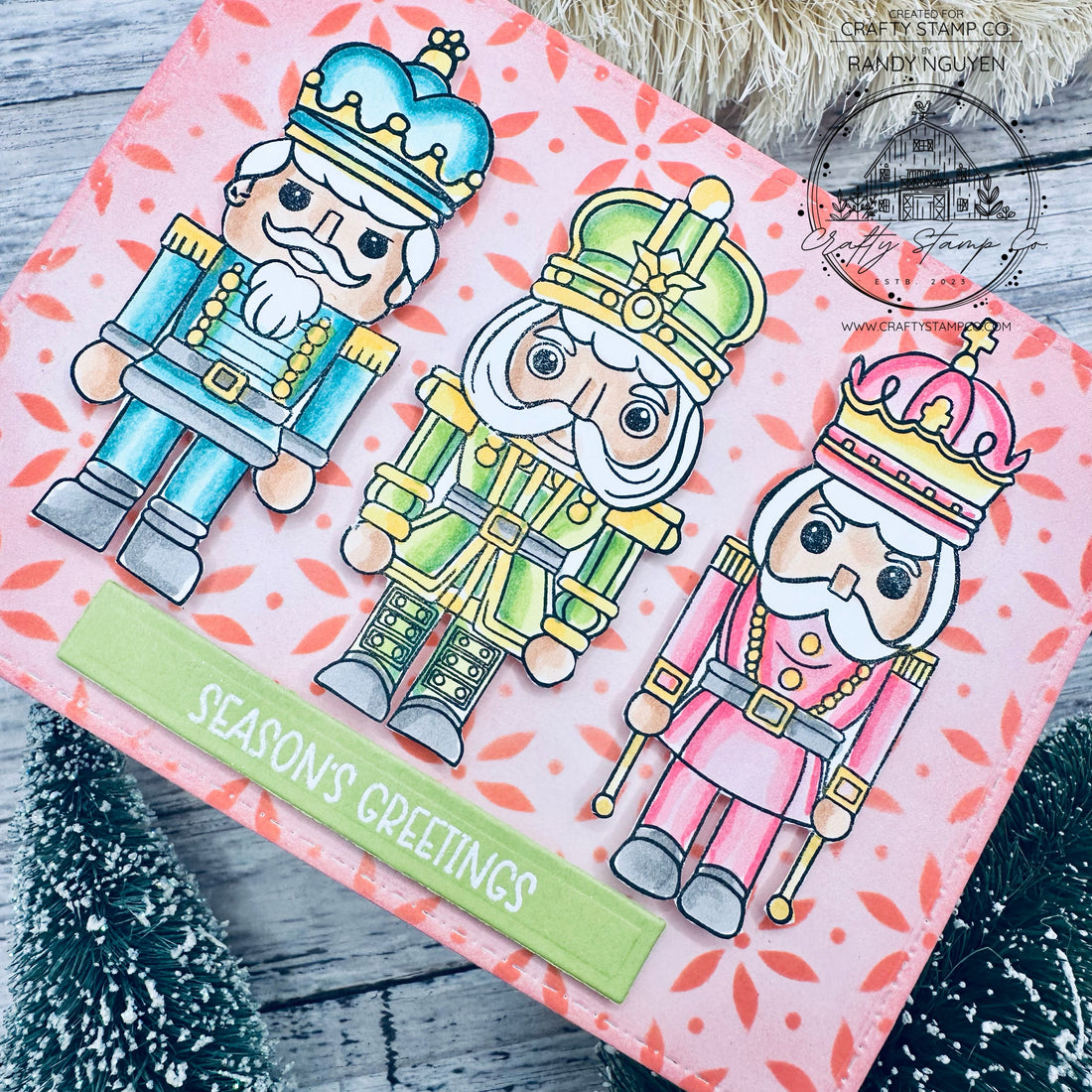 Handmade Christmas card featuring three colorful nutcracker characters with a pink poinsettia stenciled background using Crafty Stamp Co stamps and stencil.