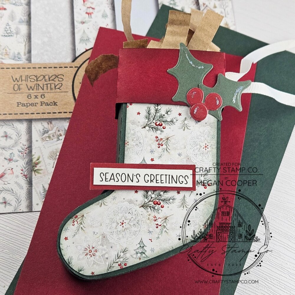 Handmade stocking-shaped gift box with holly embellishment and patterned paper, featuring the Whispers of Winter 6x6 paper by Megan.